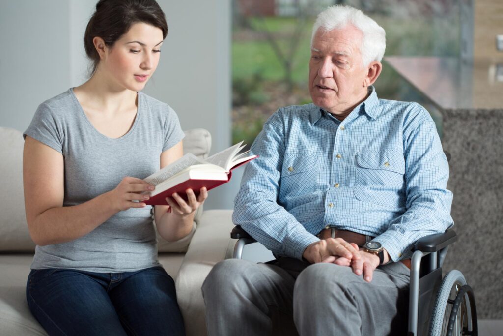 Senior care assistant reading book elderly man